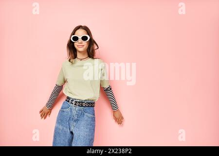 Un'elegante ragazza adolescente posa con sicurezza in una camicia verde vivace e occhiali da sole alla moda. Foto Stock