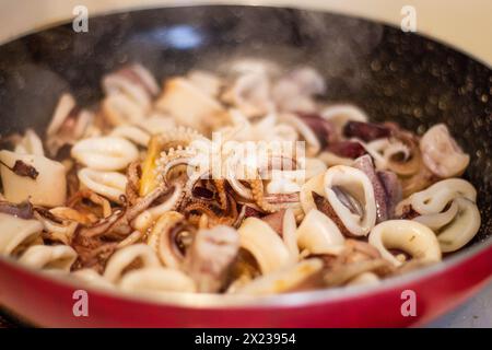 Concediti il brivido e l'aroma della frittura di calamari appena cucinata nella padella. Provate l'arte culinaria e la delizia della cucina mediterranea Foto Stock