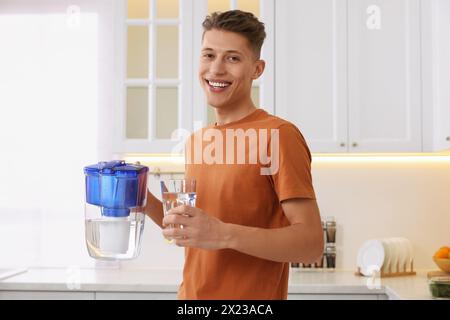 Uomo felice con caraffa filtrante e bicchiere d'acqua pulita in cucina Foto Stock