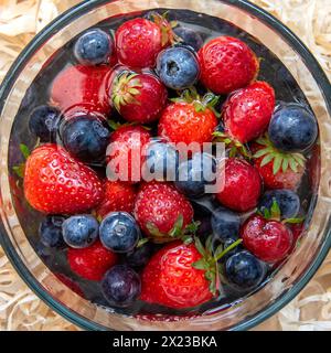 Immagine in alto di fragole e mirtilli lavati in acqua in una ciotola di vetro Foto Stock