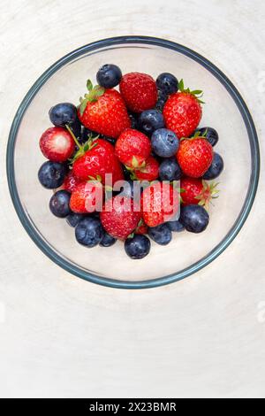 Immagine in alto di fragole e mirtilli lavati in una ciotola di vetro su un tavolo in legno Foto Stock