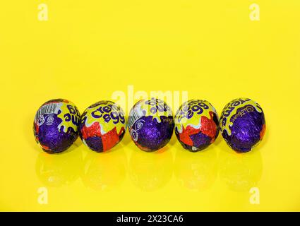 Cinque uova di crema Cadbury di fila su sfondo giallo, uova di Pasqua Foto Stock