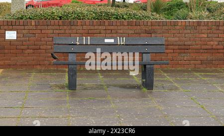 Lee-on-the-Solent, Gosport, Hampshire, Inghilterra. Aprile 2024. Una panchina pubblica sul lungomare con una starling arroccata alla fine Foto Stock