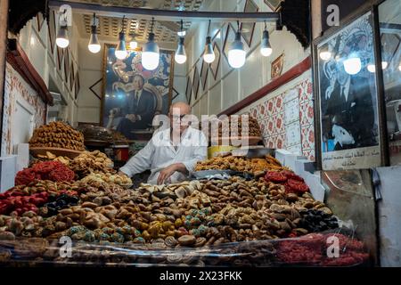Un commerciante marocchino che vende varietà di frutta secca e noci sotto i ritratti dell'ex re Hassan II e dell'attuale re Mohamed vi Foto Stock