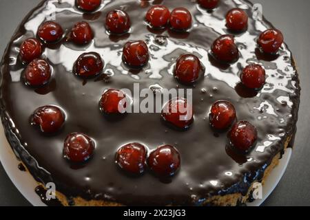 Torta bianca in spugna "ciliegia secca" decorata con glassa di cioccolato con ciliegie dolci caramellate, rosse e brillanti. Foto Stock