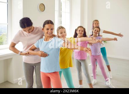Insegnante di scuola di danza per bambini aiuta le ragazze preadolescenti a eseguire esercizi coreografici. Foto Stock