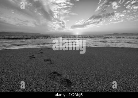 Footprints in the Sand con un paesaggio Ocean Sunrise in bianco e nero Foto Stock