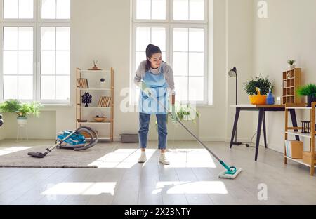 La giovane casalinga pulisce il pavimento con un panno per la pulizia a casa Foto Stock