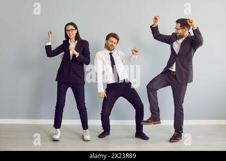 Tre uomini d'affari che ballano e celebrano il successo negli affari isolati su sfondo grigio. Foto Stock