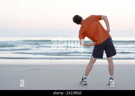 Runner che fa esercizi di stretching sulla spiaggia, Bombinhas, Santa Catarina, Brasile Foto Stock