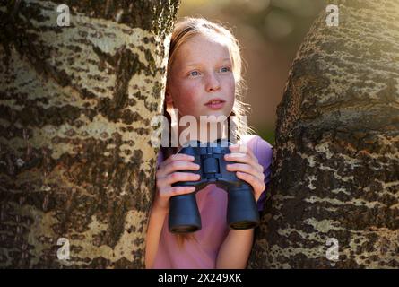 Albero, ragazza e binocolo per safari, ricerca e ricerca di animali in vacanza. Curioso, esplora e cerca il birdwatching o la fauna selvatica Foto Stock