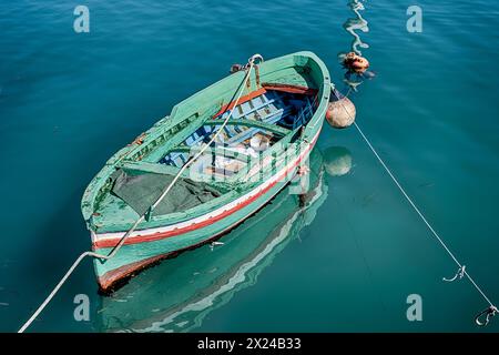 Una barca di legno verde è ormeggiata in uno dei piccoli porti di pietra della città di Siricusa, in Italia. Foto Stock