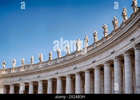 Quindici santi fiancheggiano la sommità del colonnato che racchiude il cortile principale di fronte alla basilica di San Peter a Roma. Foto Stock