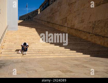 La Valletta, Malta, 4 aprile 2024. un uomo seduto sui gradini di una scala del centro città Foto Stock