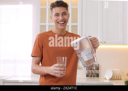 Uomo felice che versa acqua dalla caraffa del filtro in vetro in cucina Foto Stock