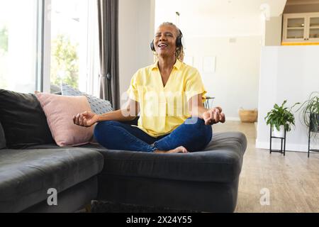 Donna afroamericana anziana seduta a gambe incrociate a casa, a meditare Foto Stock