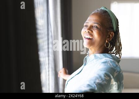Una donna afroamericana anziana con dreadlock guarda fuori dalla finestra a casa Foto Stock
