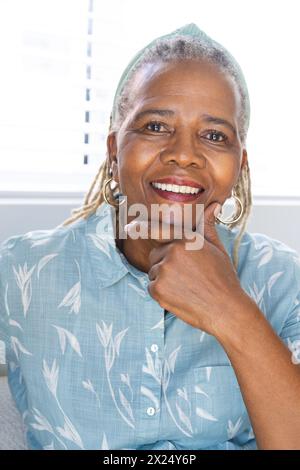 Una donna afroamericana con i capelli grigi sorride e tocca il mento a casa Foto Stock
