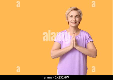 Ritratto di una donna matura meditata su sfondo giallo Foto Stock