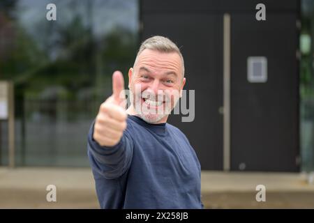 Entusiastico motivati attraente uomo di mezza età dando un pollice in alto gesto di approvazione e di successo con un sorriso raggiante Foto Stock