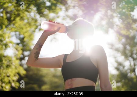 Donna attiva che beve acqua dopo l'allenamento in natura Foto Stock