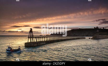 Una piccola barca da pesca che parte dal porto di Whitby all'alba. Foto Stock