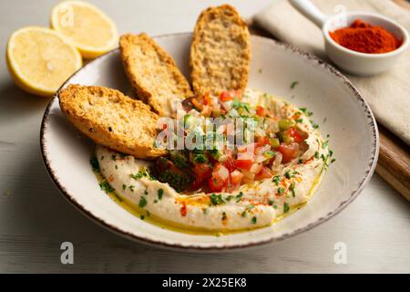 Hummus di ceci tradizionale con pepe tagliato e cipolla al centro servito con pane tostato. Foto Stock