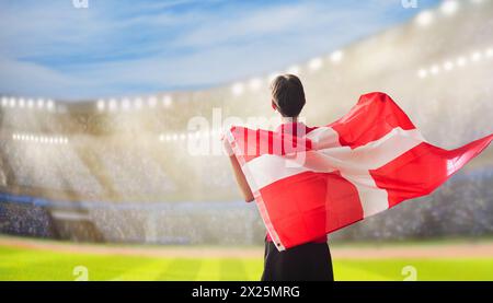 Tifoso di calcio danese allo stadio. Tifosi danesi sul campo di calcio che guardano la squadra. Gruppo di sostenitori con bandiera e maglia nazionale Foto Stock