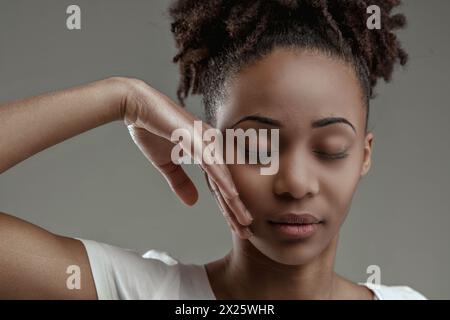 Giovane donna nera serena con gli occhi chiusi, la mano tocca delicatamente il viso Foto Stock