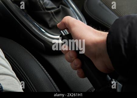 Uomo che tiene e tira la maniglia del freno a mano freno di emergenza e-Brake nell'abitacolo nero dell'auto Foto Stock