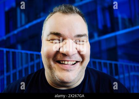 Sorriso bianco di un uomo europeo in sovrappeso di 47 anni, ritratto ravvicinato su sfondo blu. Foto Stock