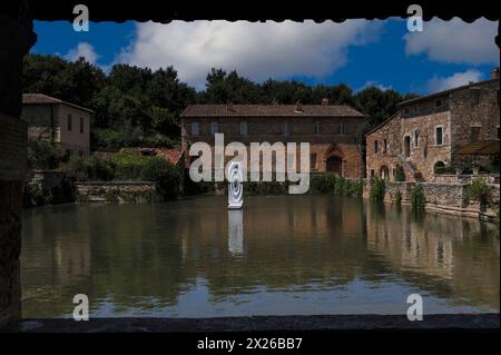 Le terme di Santa Caterina del XVI secolo a bagno Vignoni in Toscana, Italia. Una moderna opera d'arte scultorea si riflette nell'acqua calda di sorgente vulcanica che riempie una piscina rettangolare. L'acqua di bagno Vignoni, con le sue rinomate proprietà curative, ha attirato etruschi, romani, Santa Caterina da Siena, Papa Pio II e Lorenzo il magnifico. Nel tardo medioevo, il villaggio termale divenne una tappa popolare per i pellegrini cristiani che percorrevano la via Francigena verso Roma. Foto Stock