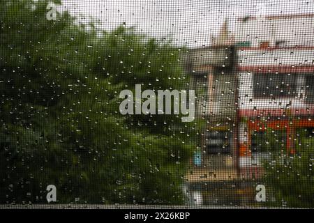 L'acqua piovana cade sulla finestra di garza con sfondo di piante ed edifici. Foto Stock