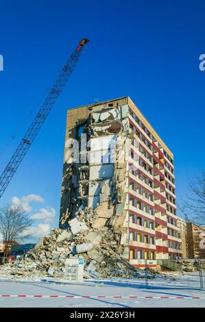 Un blocco torre parzialmente demolito si trova accanto a una gru in una giornata invernale di sole Foto Stock