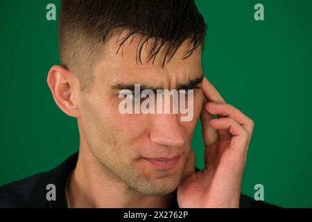 emozioni di un bell'uomo su sfondo verde cromakey primo piano capelli scuri giovane uomo. un uomo dai capelli scuri dall'aspetto gradevole guarda direttamente lo spettatore con un'espressione dura sul suo viso Foto Stock