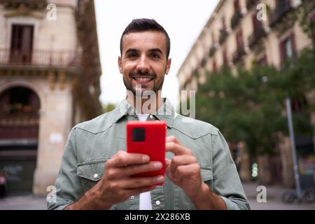 Ritratto il giovane europeo sta sorridendo davanti alla fotocamera che tiene il cellulare nella città di Madrid. Foto Stock