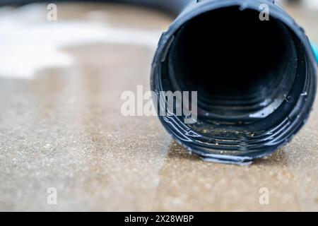 Attenzione selettiva all'apertura anteriore di una pompa di estrazione residenziale che scarica l'acqua dall'estremità di un flessibile flessibile nero Foto Stock