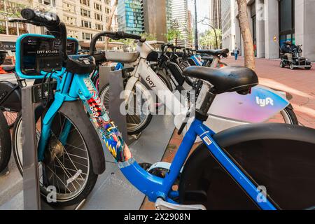 San Francisco, California, 8 aprile 2024. Le biciclette ancorate attendono i ciclisti su un marciapiede di San Francisco con la vita urbana sullo sfondo. Foto Stock
