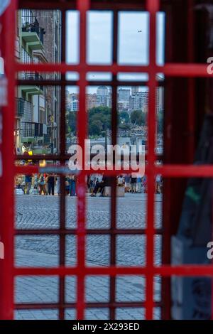 Strada turistica acciottolata a Porto al tramonto, piena di turisti che camminano con il cielo nuvoloso visto attraverso una tipica cabina telefonica rossa portoghese. Foto Stock