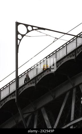 Uomo in maglietta gialla e donna vestita di nero con capelli lunghi, che cammina sulla sommità del ponte in acciaio Don Luis i a Porto con dettagli in metallo Foto Stock