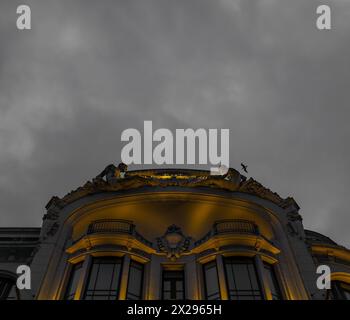 Facciata di un lussuoso edificio classico, splendidamente decorato con due sculture umane che siedono simmetricamente sul tetto illuminate da li dorati Foto Stock