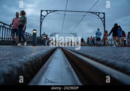 Binario in acciaio della metropolitana di Porto al piano terra del Ponte Dom Luis al tramonto, pieno di turisti che passeggiano sotto un cielo nuvoloso. Foto Stock