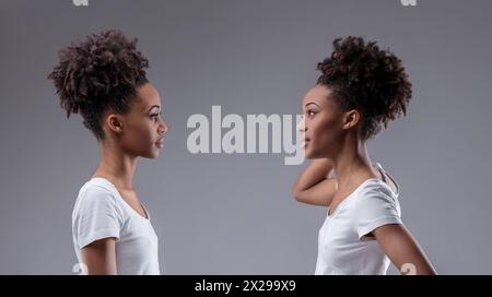Il dubbio di sé e il controllo interagiscono nella posizione di una giovane donna nera che valuta la sua riflessione Foto Stock
