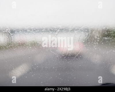 Immagine sfocata di una strada trafficata con auto e camion. La pioggia sta facendo bagnare il parabrezza delle auto e del camion Foto Stock