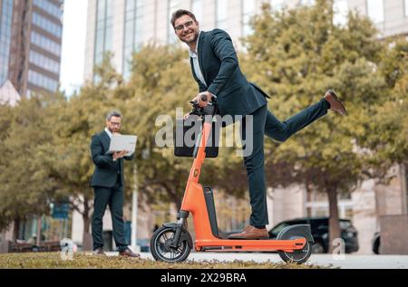 Affari pazzi, veloci e facili. Un uomo d'affari eccitato e divertente su uno scooter elettrico per le strade cittadine. Impiegato uomo d'affari avvocato aziendale in suit riding e Foto Stock