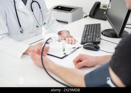 Un esperto medico si concentra sulla scrittura delle informazioni vitali in un ambiente clinico. Foto Stock