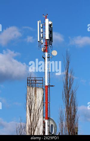 Robusto polo in metallo rosso e bianco con trasmettitori e antenne per telefoni cellulari di varie forme e dimensioni montati su ciascun lato accanto a edifici alti Foto Stock