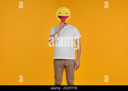 Uomo che copre il viso con emoticon che sporge la lingua su sfondo giallo Foto Stock