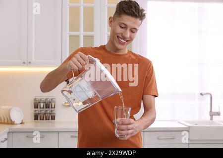 Uomo felice che versa acqua dalla caraffa del filtro in vetro in cucina Foto Stock