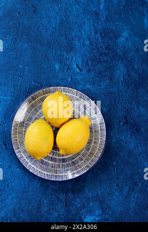 Limoni su sfondo blu. Foto a contrasto di frutta gialla su un tavolo blu testurizzato. Composizione semplice natura morta. Foto Stock